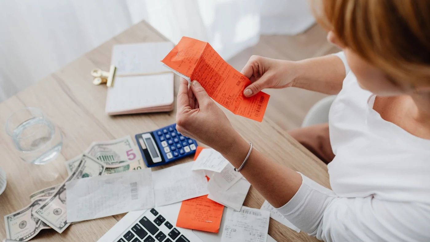 A person reviewing receipts with a calculator and laptop