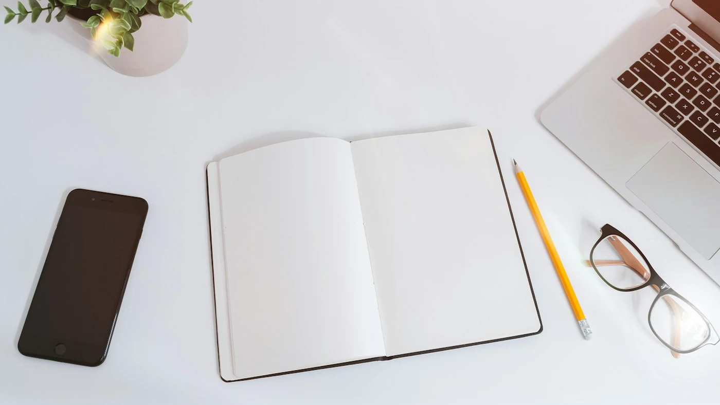 A laptop, phone and open notebook on a work desk